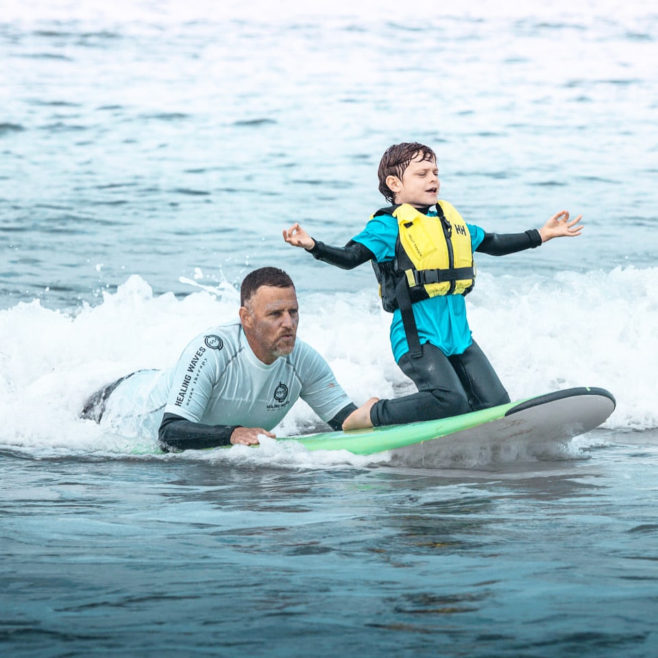 Child learning to surf with instructor at sea.