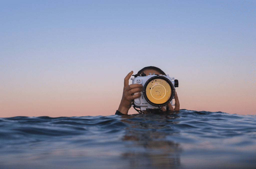 Photographer with underwater camera at sea during sunset.