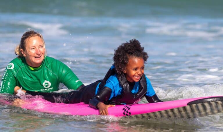 Surfing lesson with joyful instructor and child at sea.
