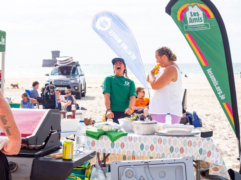 Beach event with BBQ and laughter under promotional banners.
