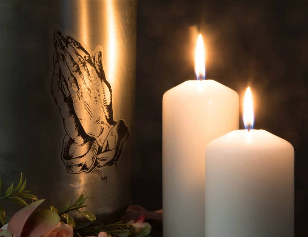 Praying hands on candle with two lit candles.