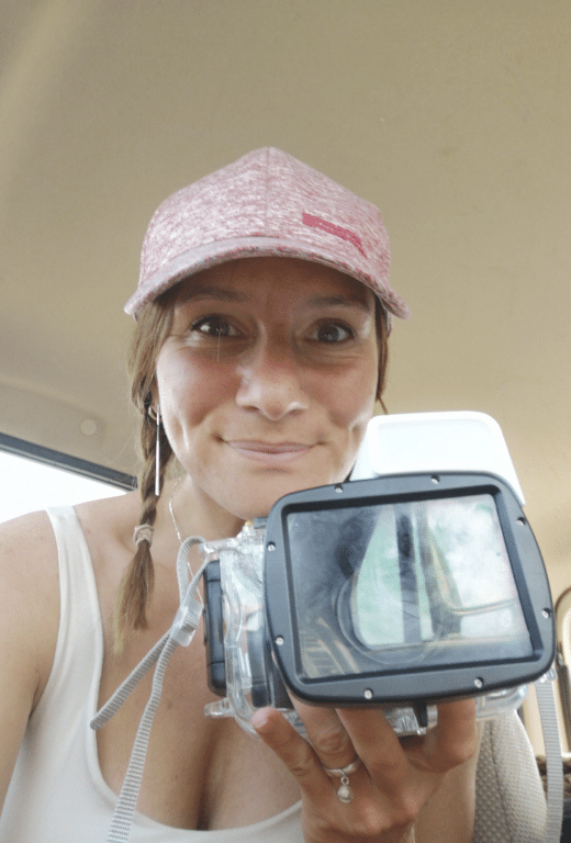 Woman holding underwater camera, wearing cap and smiling.